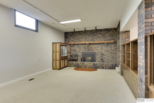 unfurnished living room featuring carpet, a wood stove, rail lighting, and brick wall