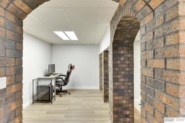 office space featuring brick wall, baseboards, a drop ceiling, and wood finished floors
