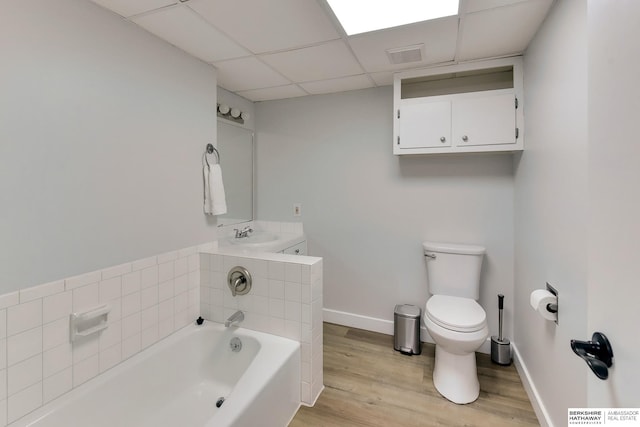 bathroom with wood finished floors, toilet, a drop ceiling, a tub, and a sink