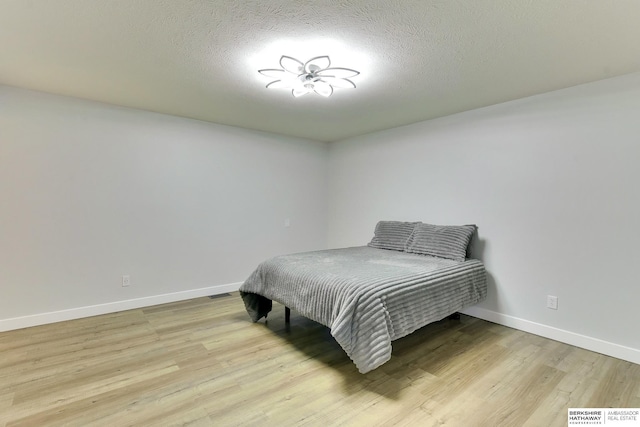 bedroom featuring a textured ceiling, baseboards, visible vents, and light wood finished floors