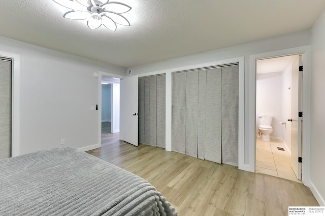 bedroom with visible vents, two closets, wood finished floors, and connected bathroom