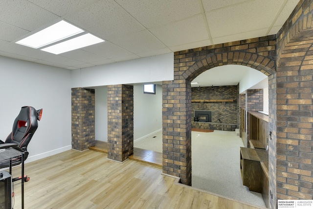 office with a fireplace, brick wall, baseboards, a drop ceiling, and wood finished floors