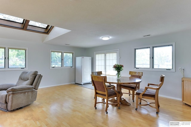 dining room featuring a skylight, visible vents, baseboards, and light wood finished floors