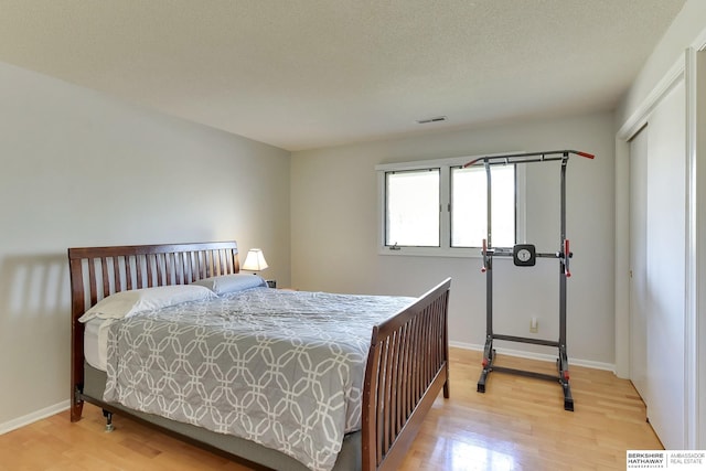 bedroom with baseboards, light wood finished floors, and visible vents