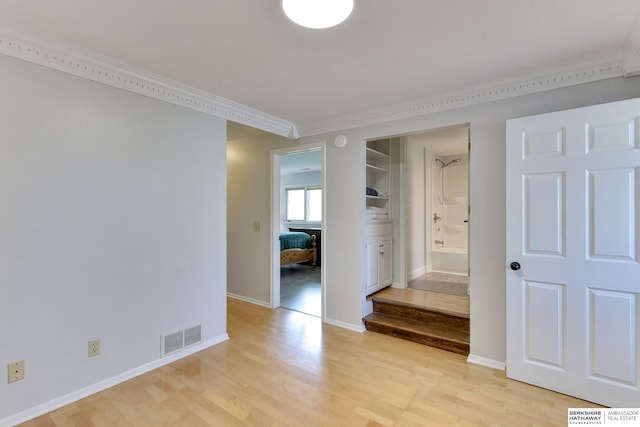 hall with ornamental molding, light wood-style flooring, and visible vents