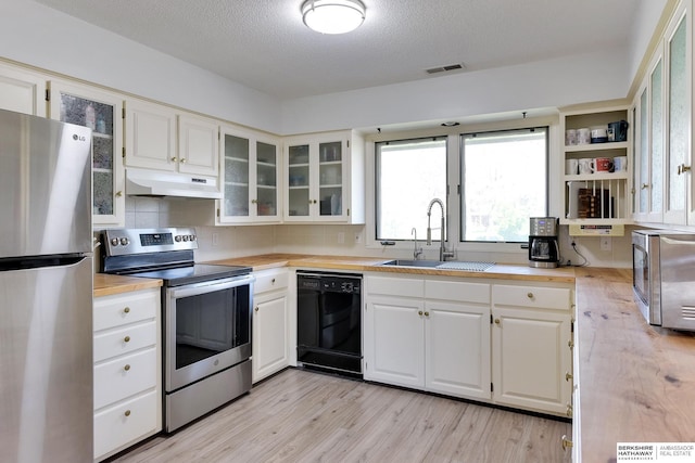 kitchen featuring visible vents, under cabinet range hood, a sink, light wood-style flooring, and stainless steel appliances