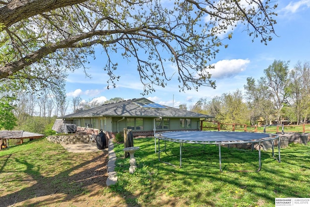 rear view of house with a lawn, a trampoline, and roof mounted solar panels
