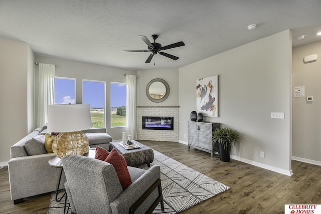 living area featuring dark wood-style flooring, a textured ceiling, baseboards, a fireplace, and a ceiling fan