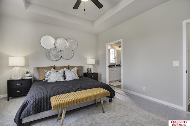 bedroom with a tray ceiling, baseboards, connected bathroom, ceiling fan, and light carpet