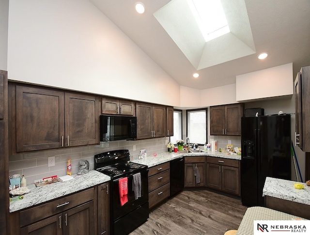 kitchen featuring dark brown cabinetry, a sink, wood finished floors, black appliances, and lofted ceiling with skylight
