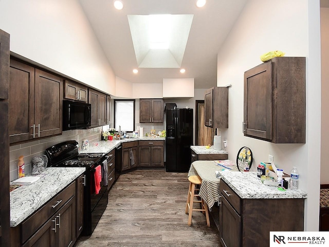 kitchen with lofted ceiling, a sink, dark brown cabinets, black appliances, and wood finished floors