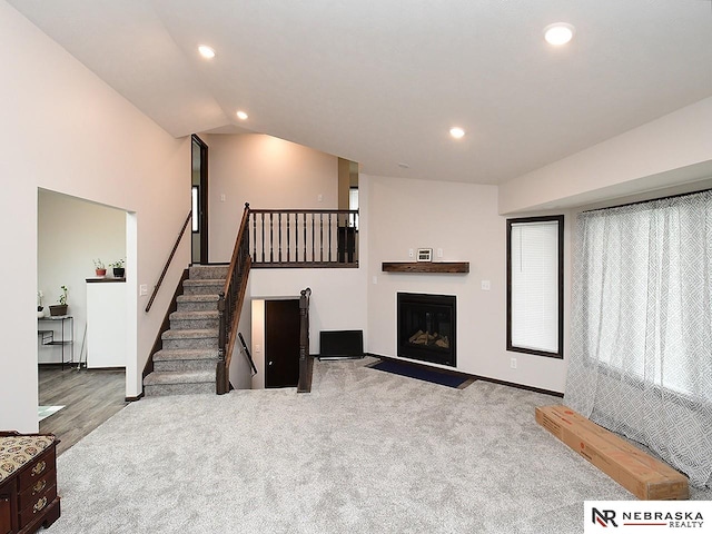 living area with baseboards, stairway, recessed lighting, lofted ceiling, and a glass covered fireplace
