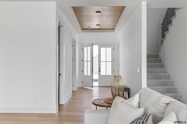 entryway featuring baseboards, stairs, a raised ceiling, light wood-type flooring, and wooden ceiling