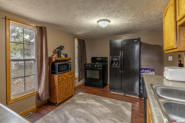 kitchen featuring a sink, dark wood-style floors, baseboards, visible vents, and black appliances