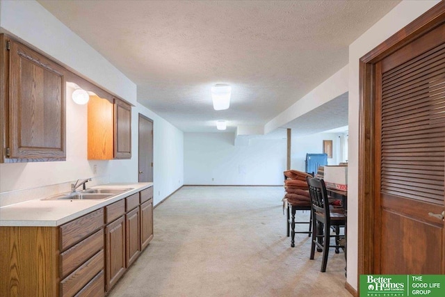 kitchen with a textured ceiling, light colored carpet, light countertops, a sink, and open floor plan