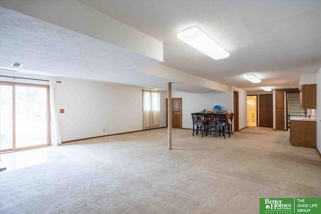 basement with a textured ceiling, a healthy amount of sunlight, and light colored carpet