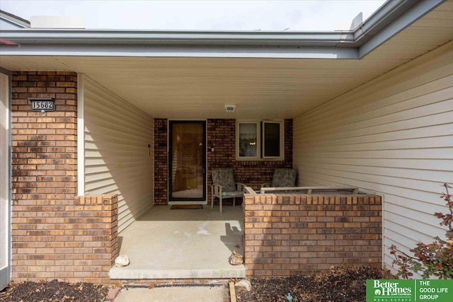 view of exterior entry featuring a porch and brick siding