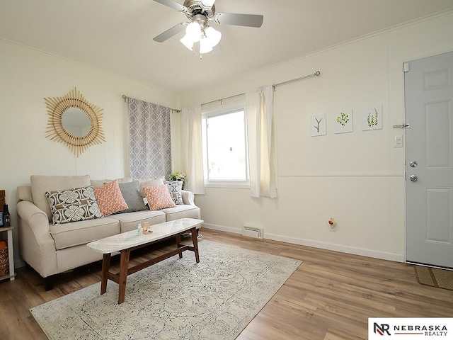 living room with a ceiling fan, ornamental molding, baseboards, and wood finished floors