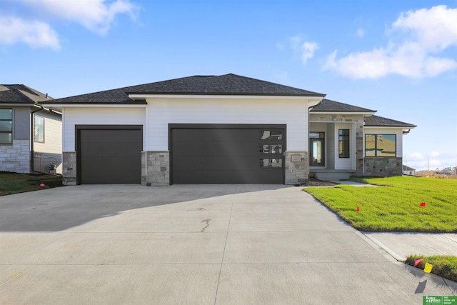 prairie-style home with an attached garage, stone siding, a front lawn, and concrete driveway