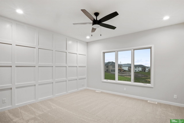 spare room featuring a decorative wall, visible vents, and light colored carpet
