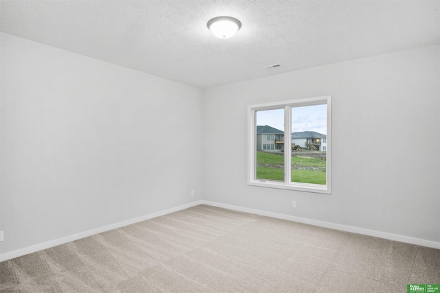 spare room featuring light carpet, baseboards, visible vents, and a textured ceiling