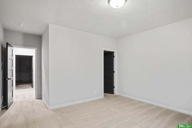 empty room with light carpet, baseboards, and a textured ceiling