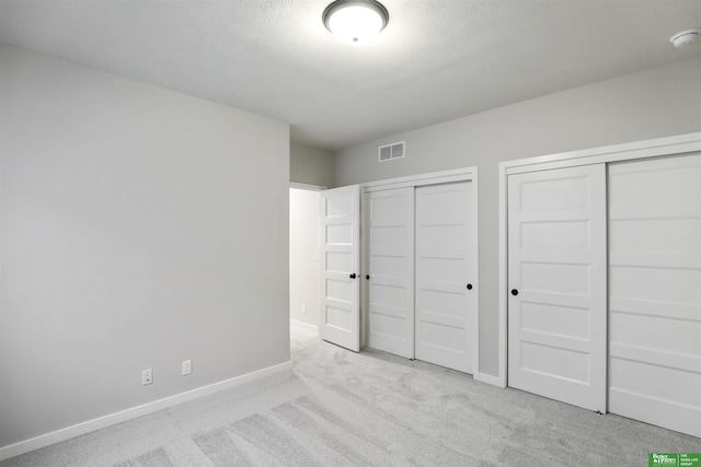 unfurnished bedroom featuring visible vents, baseboards, carpet flooring, and two closets