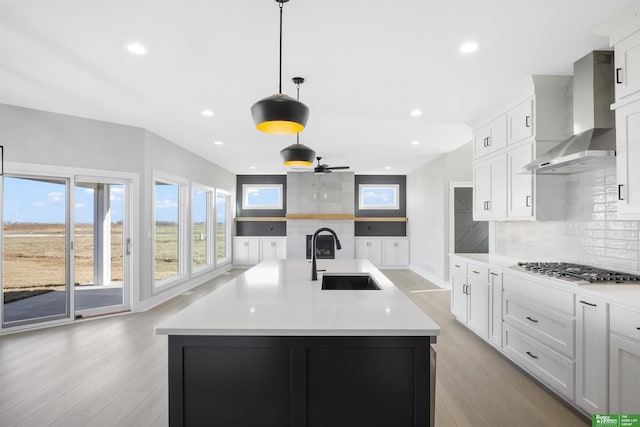 kitchen featuring tasteful backsplash, light wood-style flooring, wall chimney exhaust hood, and a sink