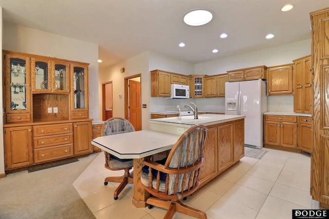 kitchen featuring recessed lighting, white appliances, glass insert cabinets, light countertops, and an island with sink