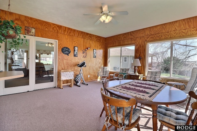 carpeted dining room with wooden walls and ceiling fan
