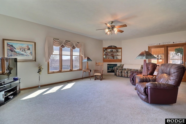 living room with ceiling fan, baseboards, a glass covered fireplace, and carpet