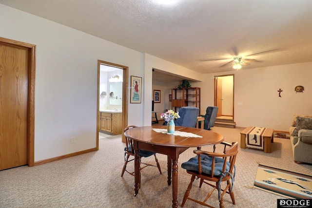 dining room featuring light carpet, baseboards, a textured ceiling, and ceiling fan