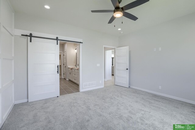 unfurnished bedroom with carpet, visible vents, recessed lighting, a barn door, and baseboards