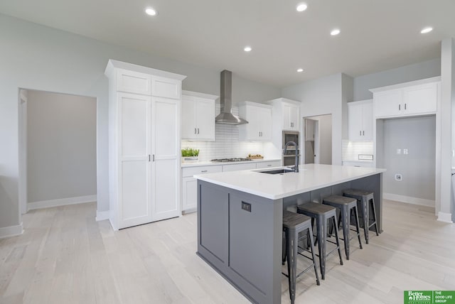 kitchen featuring light wood-style floors, wall chimney range hood, white cabinets, gas cooktop, and a large island