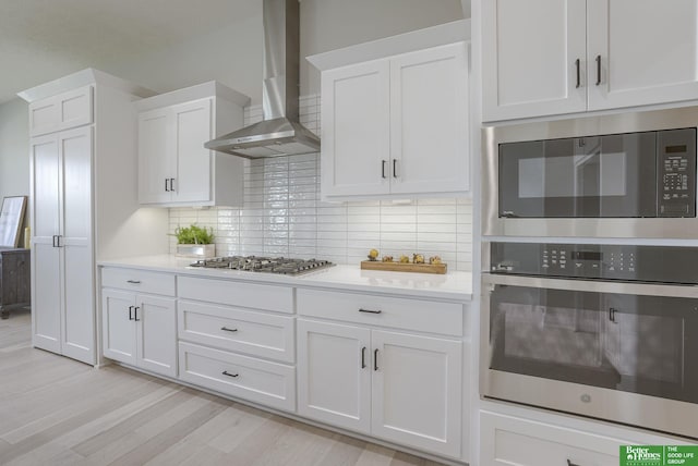 kitchen featuring light countertops, white cabinetry, wall chimney exhaust hood, and stainless steel appliances