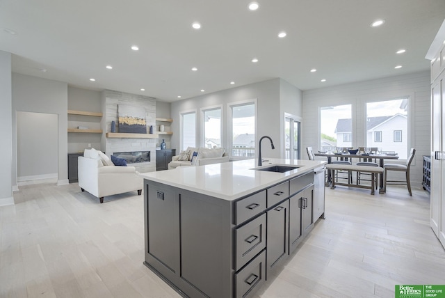 kitchen featuring a sink, light countertops, a kitchen island with sink, recessed lighting, and a large fireplace