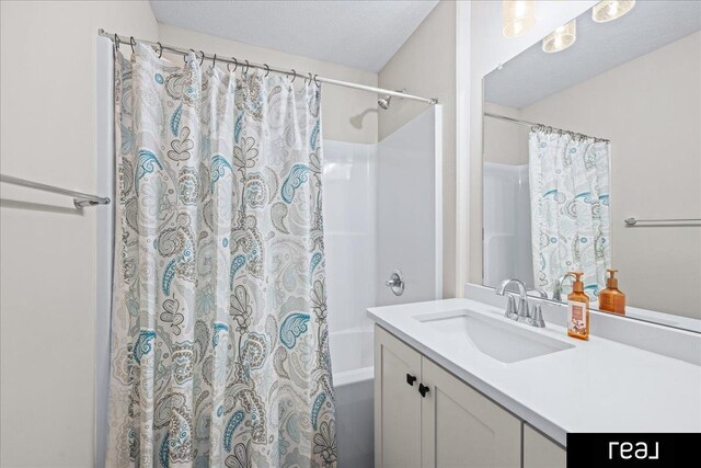 bathroom with a textured ceiling, shower / bath combo with shower curtain, and vanity
