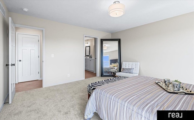carpeted bedroom with ensuite bathroom and baseboards