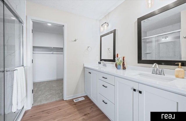 bathroom with a sink, visible vents, a walk in closet, and a stall shower