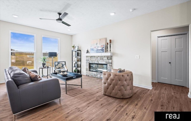 living area with baseboards, a fireplace, a textured ceiling, a ceiling fan, and wood finished floors