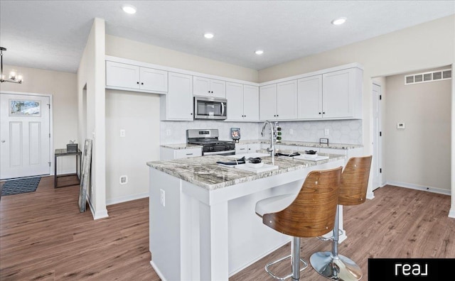 kitchen with appliances with stainless steel finishes, decorative backsplash, light stone counters, and visible vents