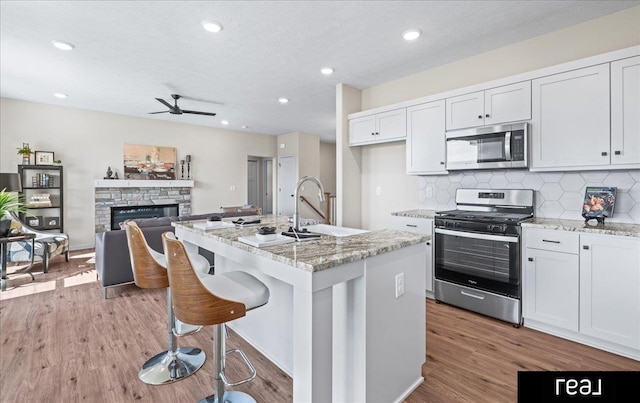 kitchen featuring a stone fireplace, a ceiling fan, decorative backsplash, stainless steel appliances, and a sink