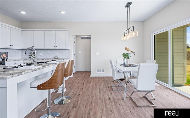 kitchen with tasteful backsplash, visible vents, a breakfast bar area, and light stone countertops