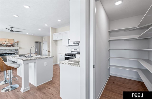 kitchen with decorative backsplash, a ceiling fan, stainless steel gas range, a sink, and light wood finished floors