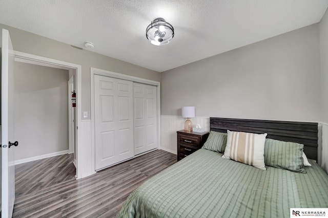 bedroom with a wainscoted wall, a textured ceiling, wood finished floors, and a closet