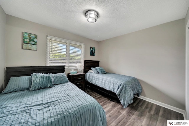 bedroom featuring baseboards, a textured ceiling, and wood finished floors