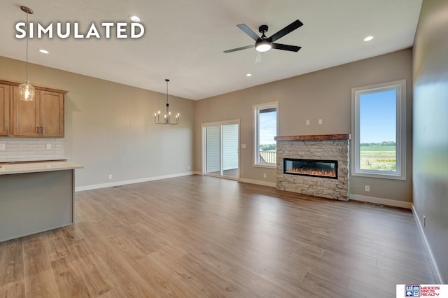 10551 Majestic Ln, Lincoln, NE 68527 - unfurnished living room with a stone fireplace, baseboards, light wood-style floors, and ceiling fan with notable chandelier
