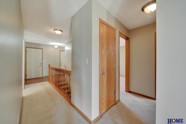 corridor with an upstairs landing, light colored carpet, and baseboards
