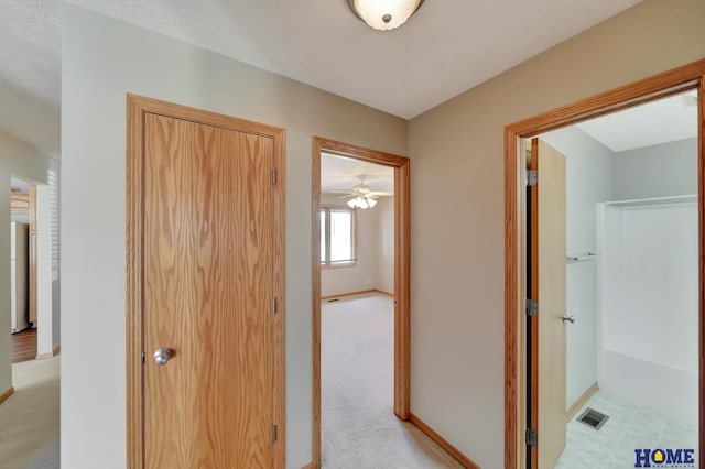 hallway with visible vents, baseboards, and light colored carpet
