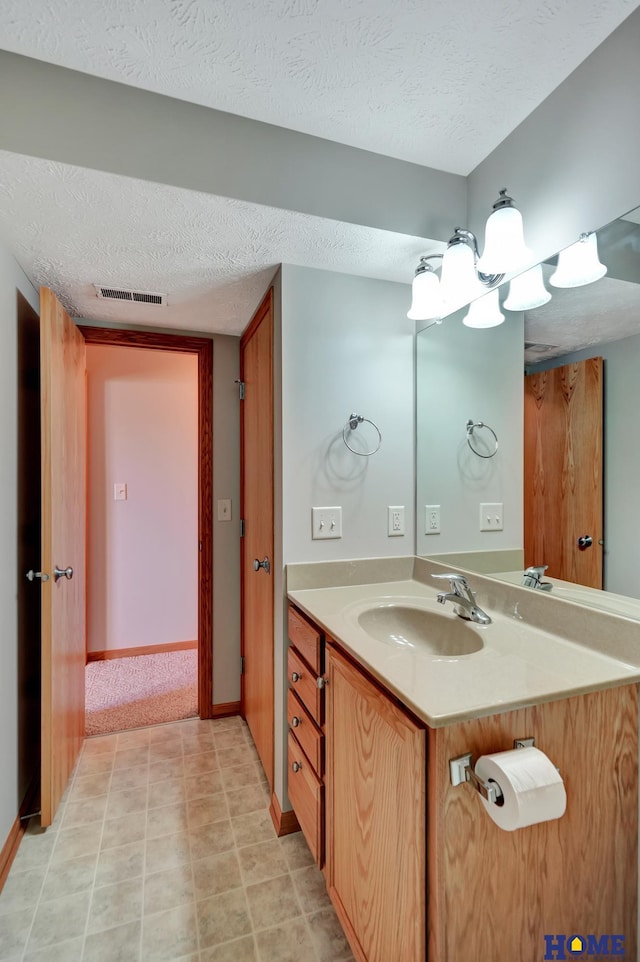 bathroom with a textured ceiling, vanity, baseboards, and visible vents